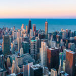 An aerial view of downtown Chicago, showcasing tall skyscrapers, bustling streets, and Lake Michigan in the background.