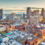 Downtown Detroit, Michigan, featuring modern skyscrapers, historic buildings, and bustling streets under a clear sky.