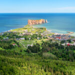 An aerial view of Percé Rock, showcasing the massive limestone formation surrounded by clear blue waters and coastline.