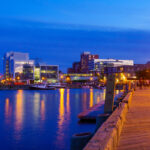 Halifax, featuring a bustling waterfront with historic buildings, boats in the harbor, and a clear blue sky.