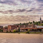 Houghton city skyline, featuring historic buildings, tree-lined streets, and the waterfront with a clear sky above.