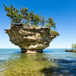 Turnip Rock in Lake Huron, a unique rock formation surrounded by clear blue waters and lush green trees.