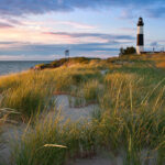 Big Sable Point Lighthouse, a tall black and white tower standing on a sandy dune, with a blue sky in the background.