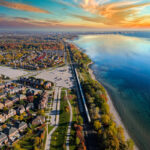 Lake Ontario coastline featuring rocky shores, clear blue waters, and lush green trees along the shoreline.