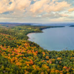 Lake Superior in autumn, featuring vibrant fall foliage along the shoreline and the calm, reflective waters of the lake.