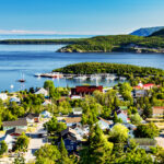 Tadoussac, Quebec, Canada, featuring picturesque buildings, a scenic waterfront, and lush green hills in the background.