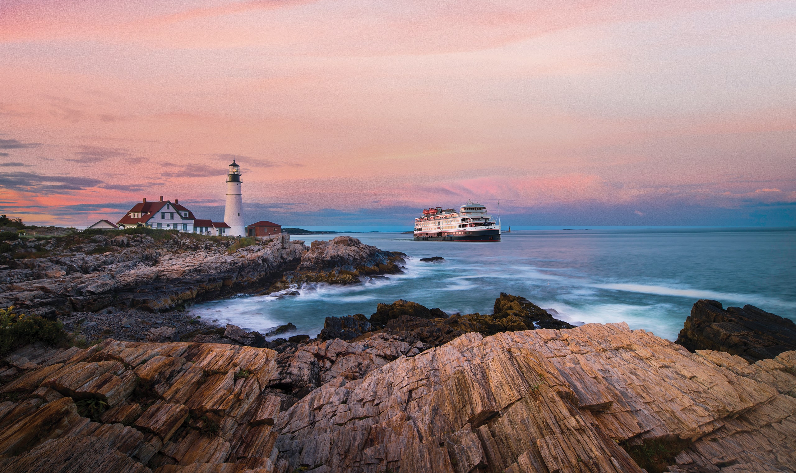 A panoramic view of a Victory Cruise Lines ship sailing smoothly off the coast, with a lighthouse standing on the nearby land.