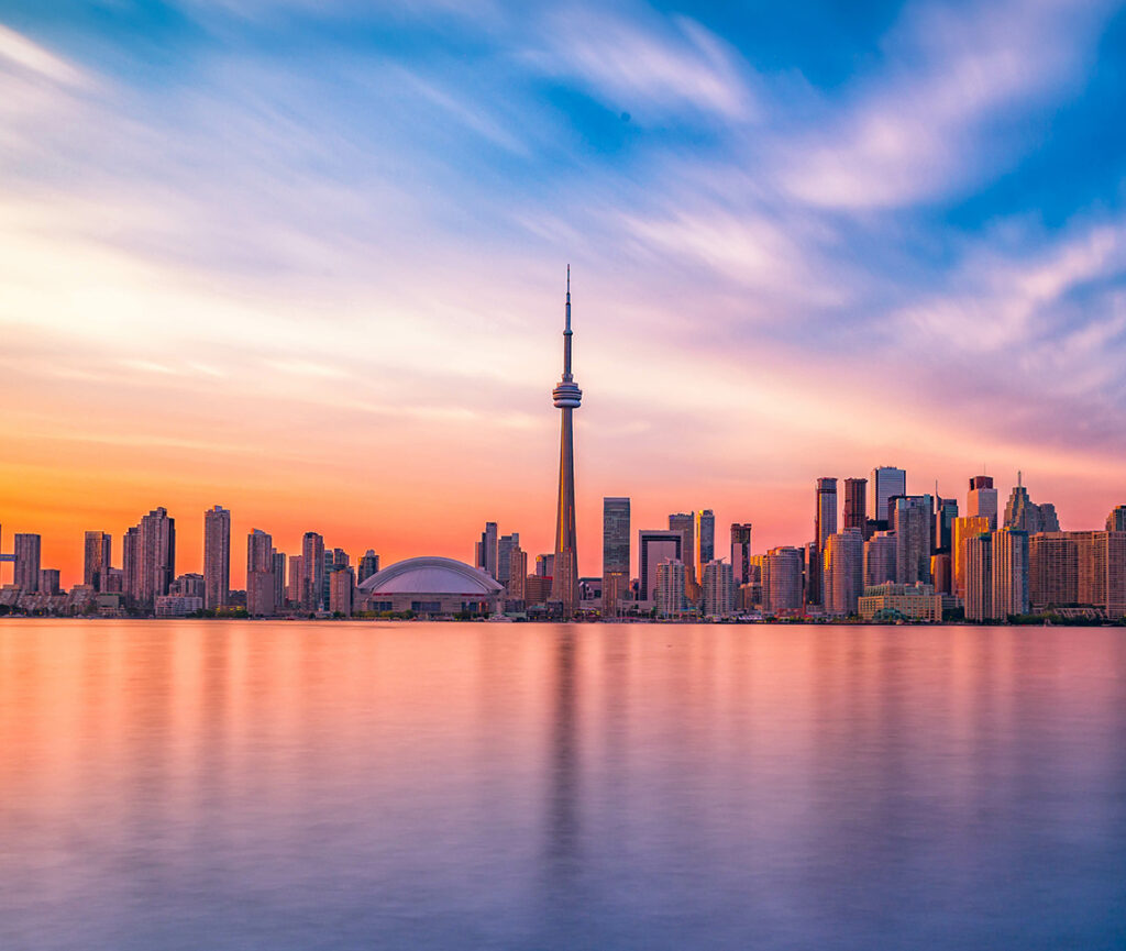 A stunning view of Toronto's skyline at sunset, with the CN Tower and skyscrapers silhouetted against a painted sky.