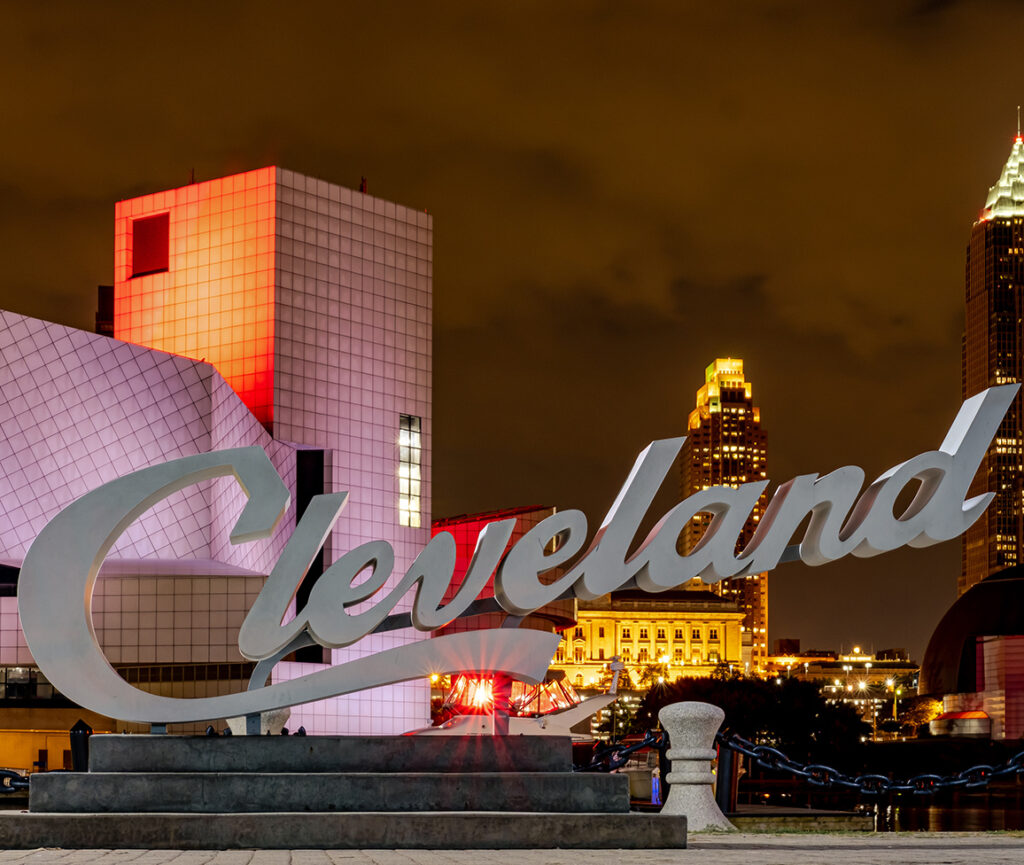 A picture of the Cleveland script sign in North Coast Harbor, with the city's skyline and Lake Erie in the background.