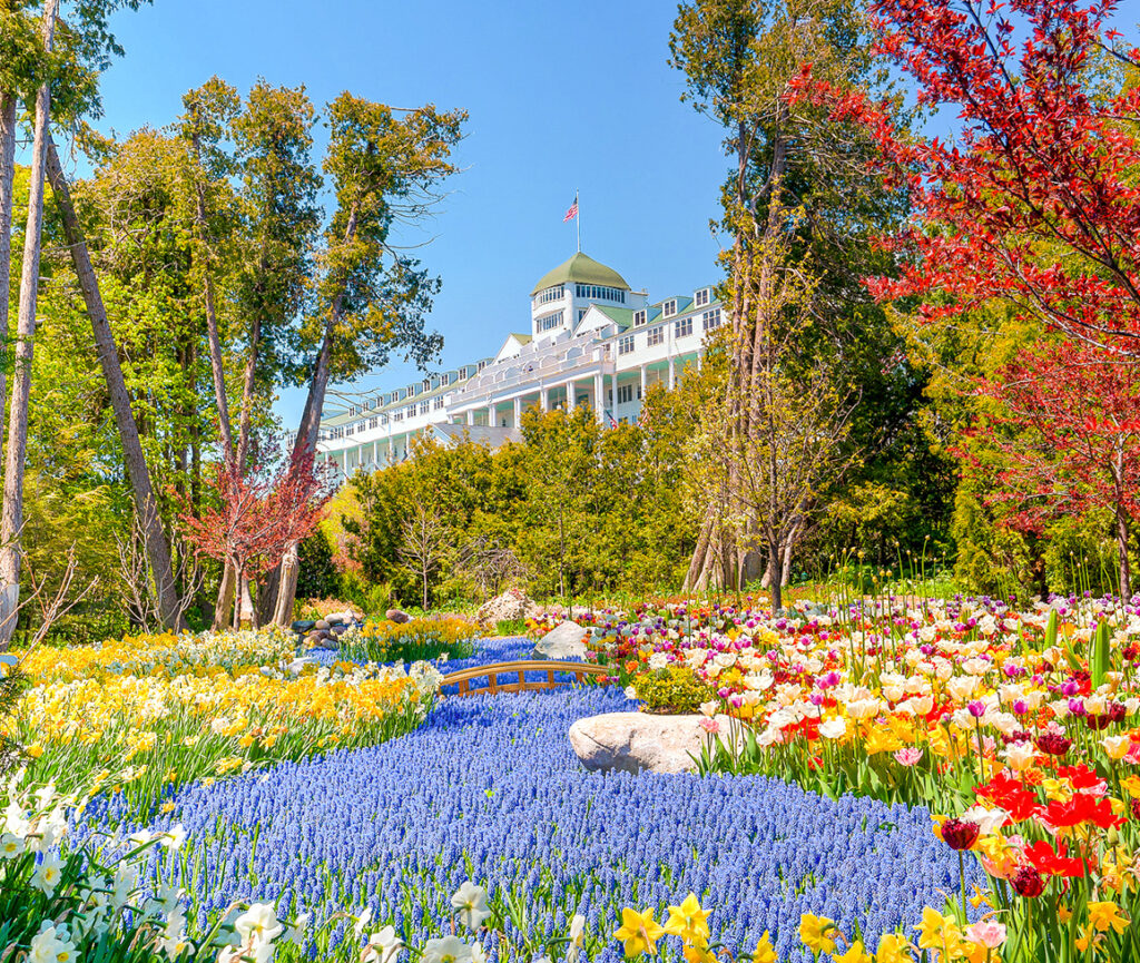 A picture of the Grand Hotel in Mackinac, featuring its grand porch, surrounded by lush gardens and vibrant flowers.