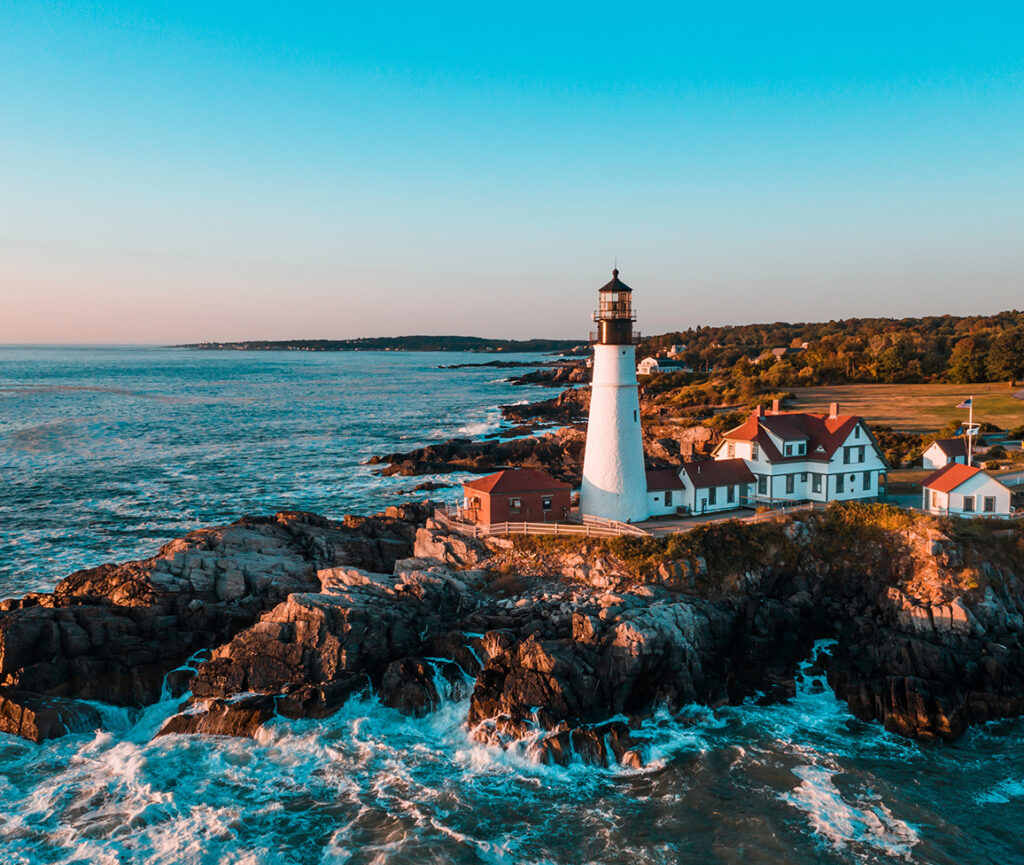 A picturesque view of Portland Head Lighthouse, perched on a rocky coastline with the ocean waves crashing below.