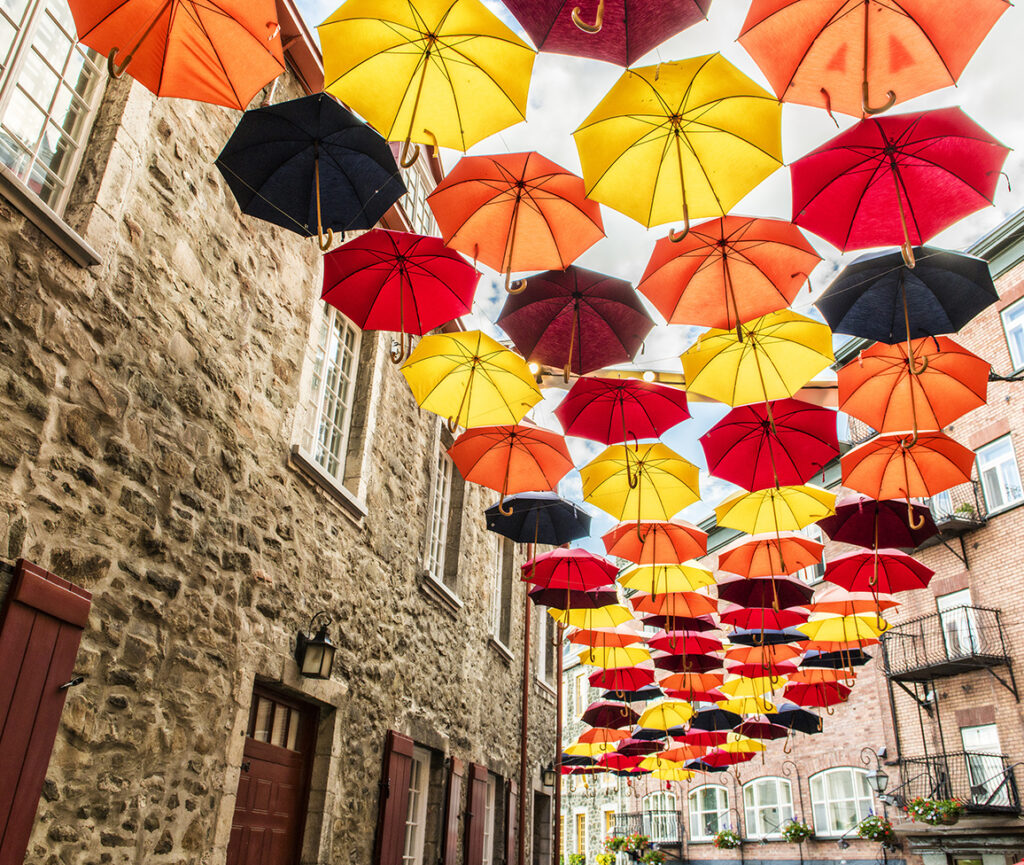 A colorful view of Petit Champlain Street, with vibrant umbrellas hanging overhead, creating a whimsical atmosphere